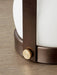 Close-up of the bronzed brass Carrie Table Lamp, detailing the textured brass knob and opal glass shade on a wooden surface.