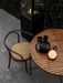 A lit Carrie Table Lamp on a wooden patio table with black dinnerware, next to a bentwood chair and an outdoor fireplace.