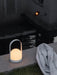 A white, illuminated Carrie Table Lamp rests on the stone edge of a swimming pool at night, a light grey towel next to it.