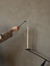A hand uses a black candle snuffer to extinguish a tall, cream tapered candle in the black Interconnect Candle Holder.