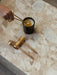 A person trims a candle wick with a brass trimmer from the Candle Care Kit. The set sits on a veined marble surface.