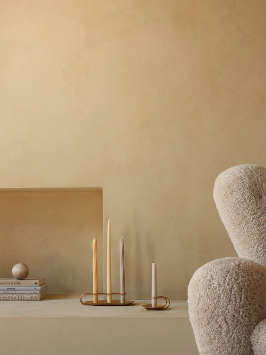 Brass Clip and Table Spire Candle Holders with tapered candles sit on a shelf beside books and a boucle Tired Man armchair.