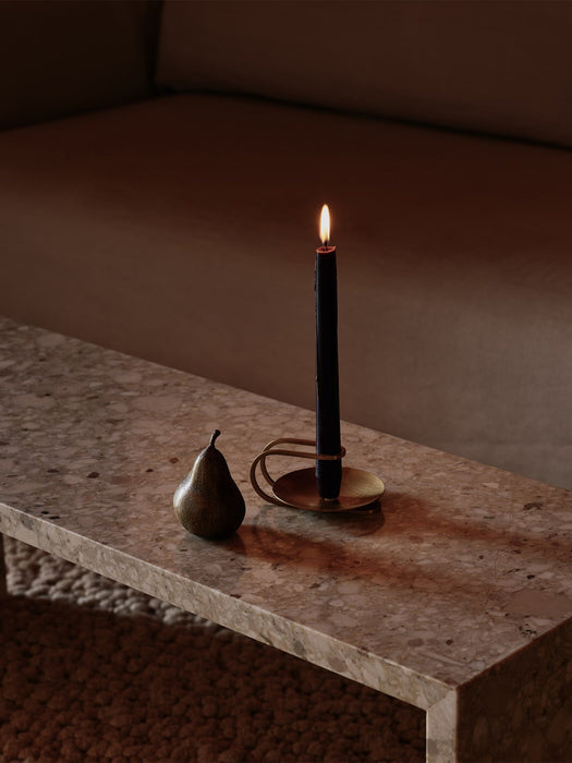 A lit black candle in a brass Clip Candle Holder and a pear-shaped Sentiment Paper Weight on a marble Plinth Bridge table.