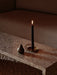 A lit black candle in a brass Clip Candle Holder and a pear-shaped Sentiment Paper Weight on a marble Plinth Bridge table.