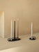 Two black metal Clip Candle Holders. One holds three lit Spire candles, and the other holds one lit Twist candle.