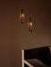 Two minimalist black Clip Candle Holder Wall sconces from Audo CPH, their lit candles casting a warm glow on a brown wall.