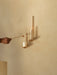 Two brass Clip Candle Holder Wall on a beige wall. A hand uses a snuffer to extinguish one candle, while the other is lit.