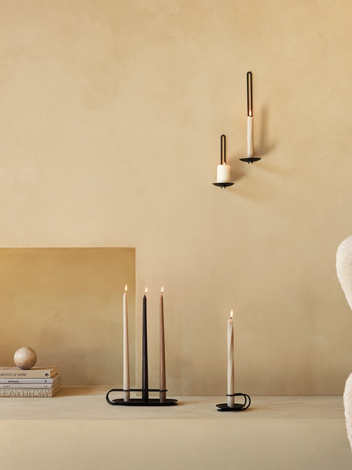 Black Clip Candle Holders on a wall and table with lit Spire and Smooth Tapered Candles in a minimalist, beige-toned room.