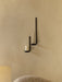 The black Clip Candle Holder mounted on a tan wall. It holds two white candles at staggered heights above a cream armchair.