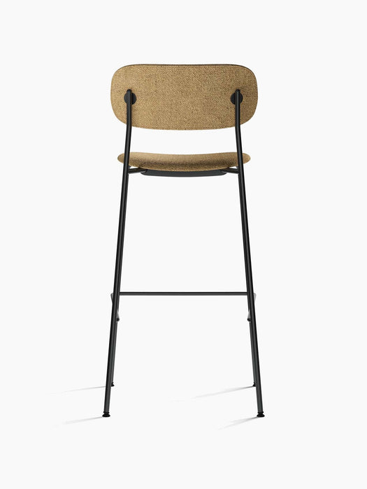 Rear view of the Co Bar Chair in light brown bouclé fabric. The chair has a slender, tubular black steel frame and footrest.
