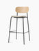 Front-angle view of the Co Bar Chair with natural oak backrest, light grey upholstered seat, and black steel frame.