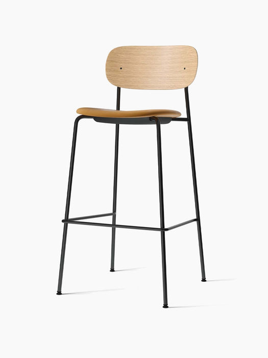 Angled view of the Co Bar Chair, Seat Upholstered, with a natural oak back, tan seat and black steel frame.
