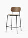 An angled view of the Co Bar Chair, featuring a dark stained oak backrest, a light bouclé seat, and a black steel frame.