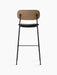 Back view of the Co Bar Chair with a dark stained oak backrest, a black upholstered seat, and a slender black steel frame.