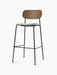An angled view of the Co Bar Chair with a dark stained oak back, upholstered seat, and a slender black steel frame.