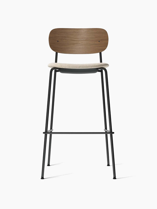A front view of the Co Bar Chair with a dark stained oak backrest, a cream upholstered seat, and a slender black steel frame.