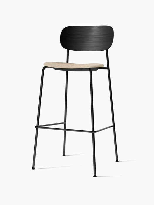 Angled view of the Co Bar Chair with a black oak backrest, beige bouclé upholstered seat, and a slender black steel frame.