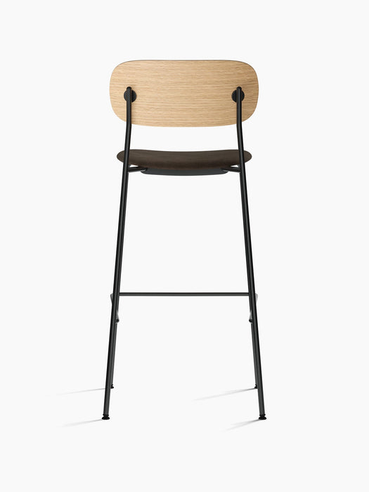 Back view of the Co Bar Chair, Seat Upholstered, showing natural oak backrest, dark upholstered seat, and black steel frame.