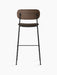 Back view of the Co Bar Chair with a dark stained oak backrest, upholstered seat, and a slender black steel frame.