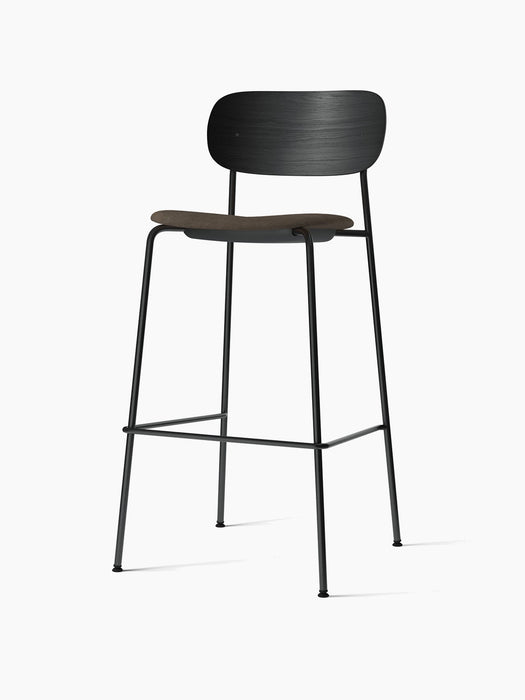An angled view of the Co Bar Chair with a black oak backrest, a dark upholstered seat, and a slender black steel frame.