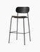 An angled view of the Co Bar Chair with a black oak backrest, a dark upholstered seat, and a slender black steel frame.