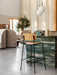 A Co Bar Chair in oak at a green marble bar. In the background are a Tearoom Sofa, Lounge Chair, and a potted plant.