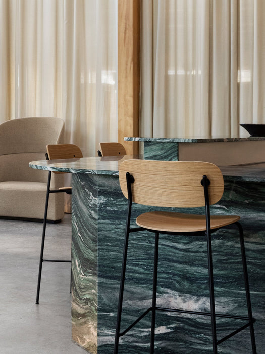 Three Co Bar Chairs with natural oak seats at a green marble kitchen island, with a beige Tearoom Sofa in the background.