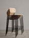 A stack of four Co Bar Chairs in natural oak veneer with black steel frames, shown against a plain grey wall.