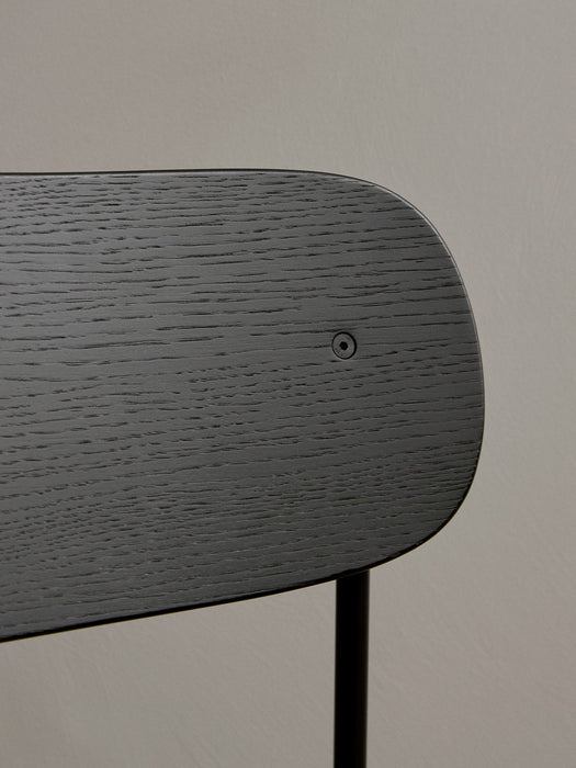 A close-up view of the Co Bar Chair's backrest in black stained oak veneer, highlighting the rich wood grain and screw.