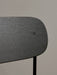 A close-up view of the Co Bar Chair's backrest in black stained oak veneer, highlighting the rich wood grain and screw.
