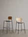 A Co Bar Chair and Co Counter Chair with natural oak veneer seats and black steel frames standing against a plain grey wall.