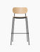 A front view of the Co Bar Chair, Veneer, with a natural oak backrest and seat on a slender, powder-coated black steel frame.