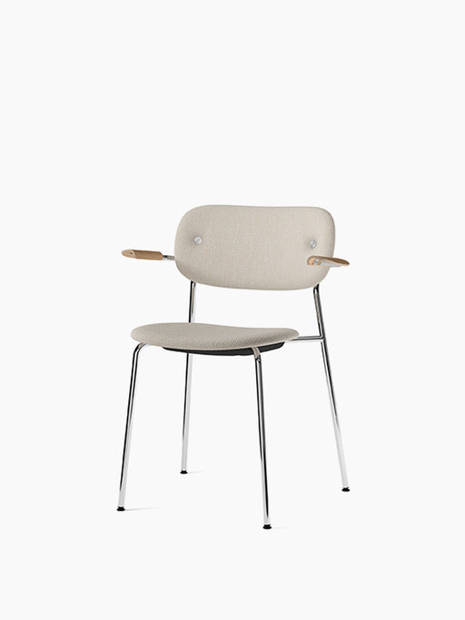 Angled view of the Co Dining Chair, fully upholstered in light beige fabric with natural oak armrests and a chrome frame.