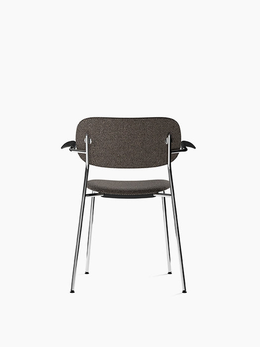 Back view of the Co Dining Chair, fully upholstered with armrest. Chrome frame, dark upholstery, and black oak armrests.
