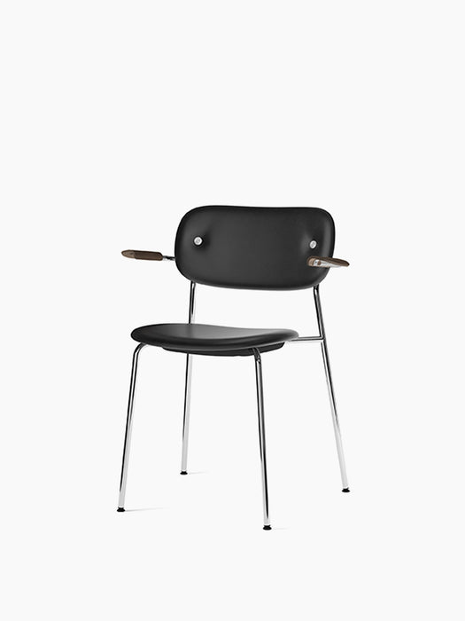 An angled view of the Co Dining Chair, fully upholstered in black leather with dark stained oak armrests and a chrome frame.