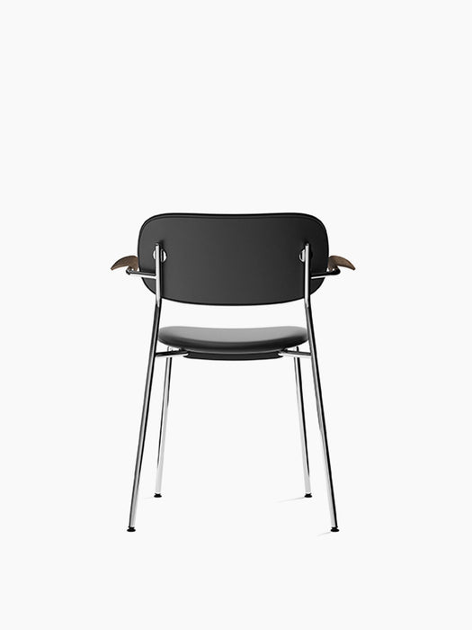 Rear view of the Co Dining Chair with black upholstery, dark stained oak armrests, and a slender chrome frame.