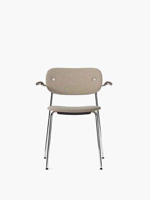 Front view of the Co Dining Chair with armrests, sand upholstery, dark stained oak armrests, and a chrome frame.