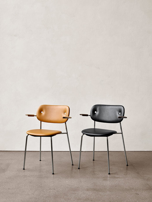 Two Co Dining Chairs with armrests and chrome frames. One is upholstered in tan leather and the other in black leather.