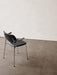 A back three-quarter view of the Co Dining Chair with black upholstery, wooden armrests, chrome frame on a concrete floor.