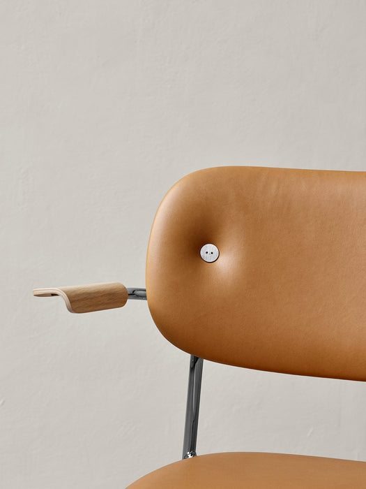 Close-up detail of the fully upholstered Co Dining Chair with armrest, tan leather back, wood armrest, and chrome frame.