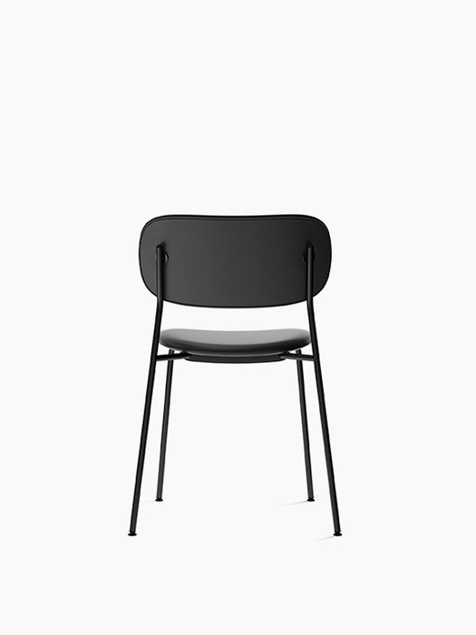 Back view of the fully upholstered black Co Dining Chair. It has a slim, black powder-coated steel frame and is armless.