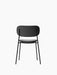 Back view of the fully upholstered black Co Dining Chair. It has a slim, black powder-coated steel frame and is armless.