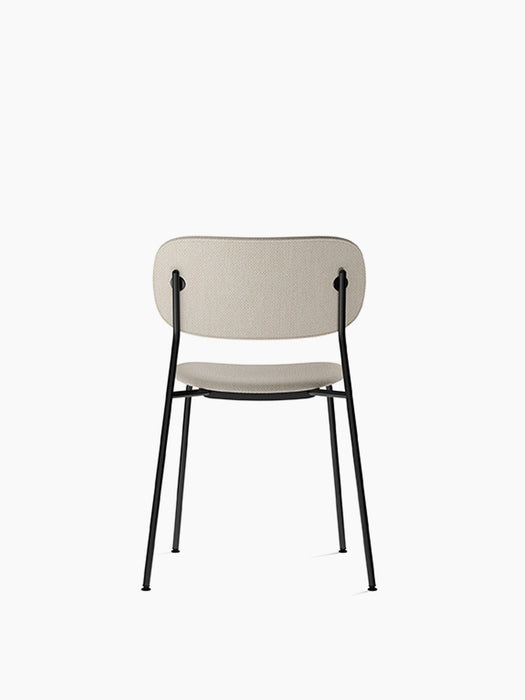Rear view of the fully upholstered Co Dining Chair in Black, showing its light beige fabric and slender black steel frame.