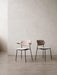 Two fully upholstered Co Dining Chairs with black legs stand on a concrete floor against a textured, off-white wall.