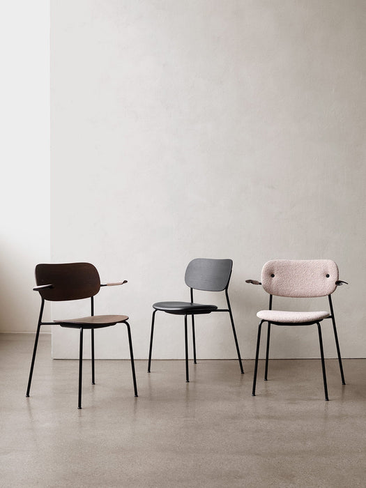 Front view of three Co Dining Chairs against a light wall: one in dark wood, one in black, and one fully upholstered in pink.