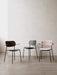 Front view of three Co Dining Chairs against a light wall: one in dark wood, one in black, and one fully upholstered in pink.