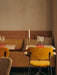 A restaurant with yellow Co Dining Chairs at tables beside an Eave Dining sofa. An Umanoff Candle Holder sits on one table.