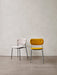 Two fully upholstered Co Dining Chairs. One in off-white bouclé with a black frame, one in yellow with a chrome frame.