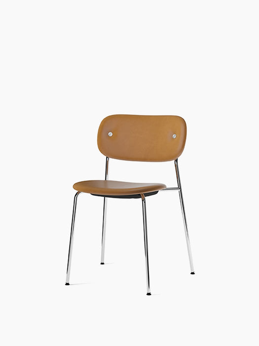 The Co Dining Chair shown at an angle, featuring tan leather upholstery on the seat and back, set on a slender chrome base.