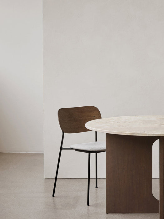 A Co Dining Chair with dark wood back, grey upholstered seat, and black frame next to a round table with a stone top.